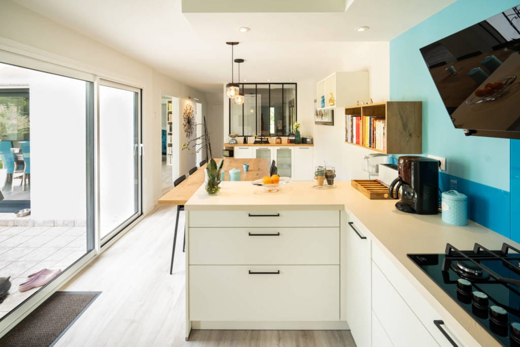 cuisine rénovée moderne bleu avec grand ilot de repas touche industriel et verrièredans une maison à Quimperlé avec canapé bleu canard et jaune moutarde